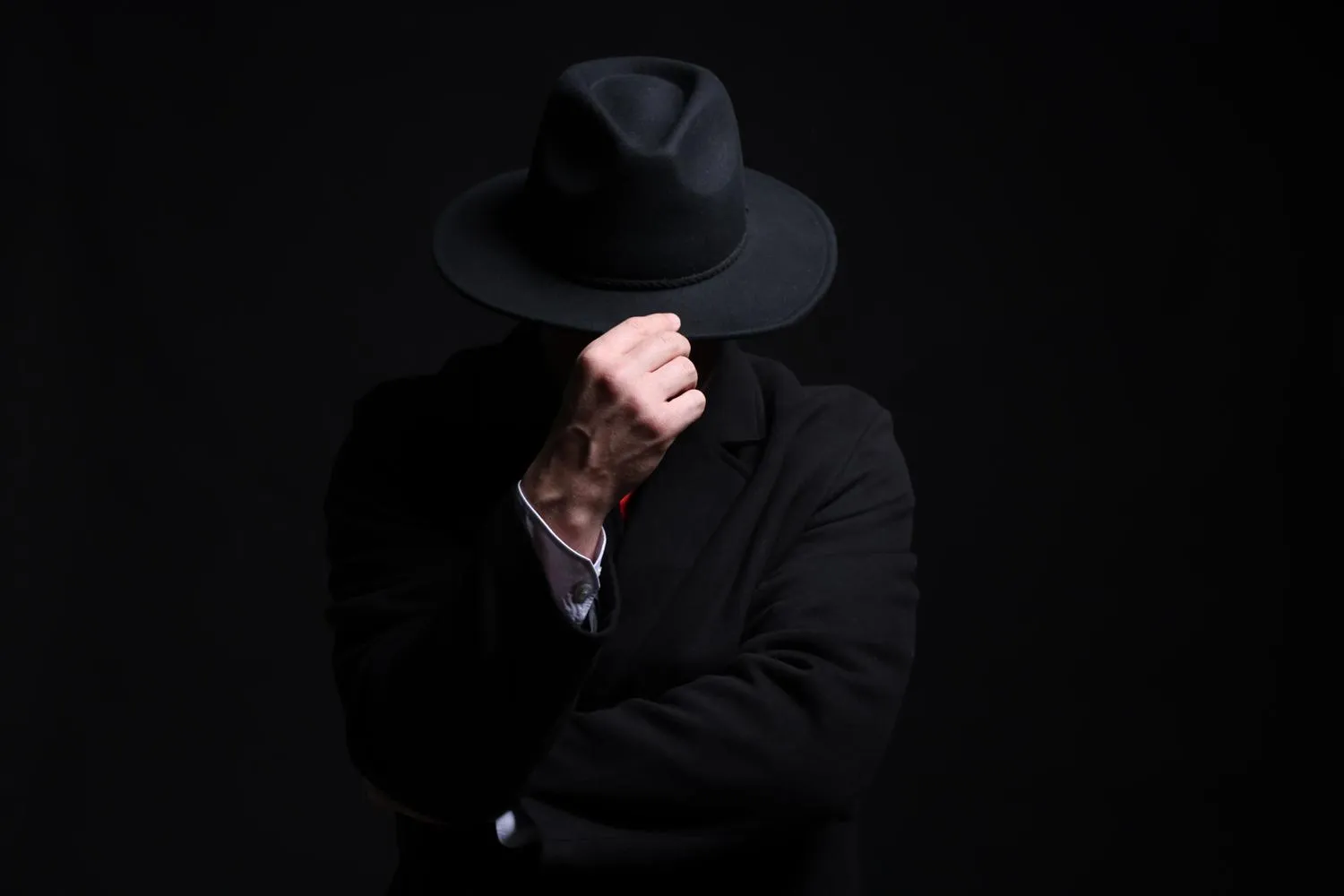 Pessoa de terno escuro e chapéu preto cobrindo o rosto, em fundo escuro, representando o black hat SEO
