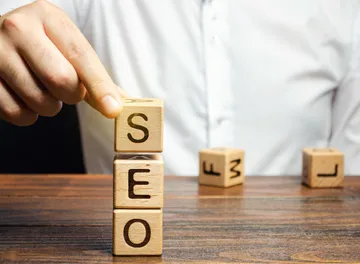 Mão empilhando cubos de madeira que formam a palavra SEO sobre uma mesa