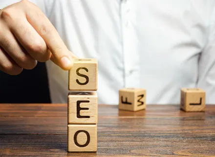 Mão empilhando cubos de madeira que formam a palavra SEO sobre uma mesa